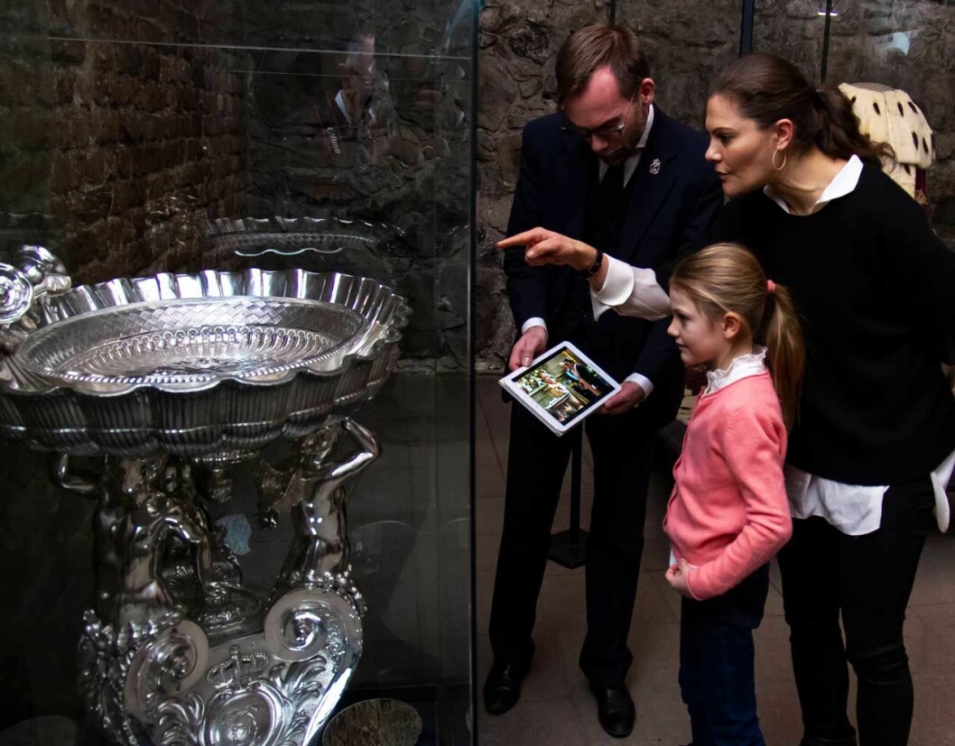 Prinsessan Estelle och kronprinsessan Victoria framför silverdopfunten i Skattkammaren på Kungliga slottet.