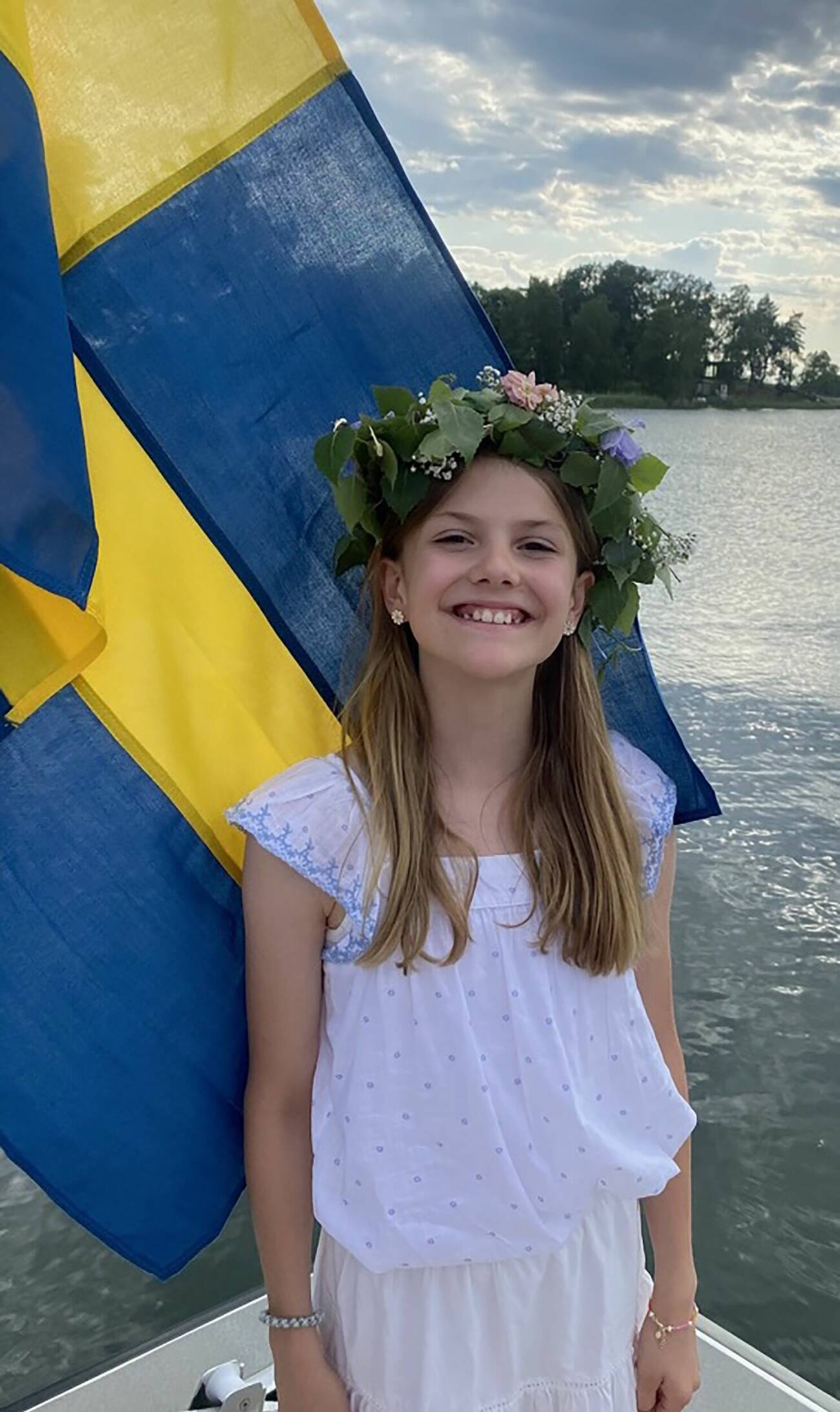 Prinsessan Estelle med en blomsterkrans och en Sverige-flagga i bakgrunden
