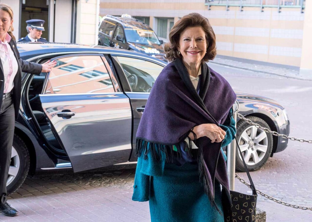 Drottning Silvia i fin blå kappa med överhängande lila sjal.