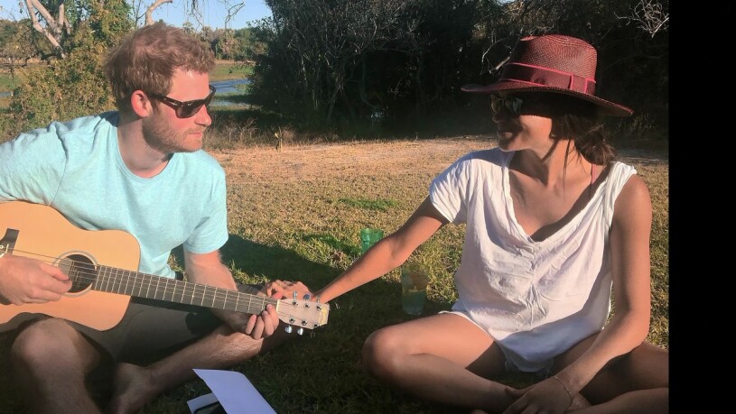 Ja, så här skulle vi nog aldrig se William och Kate. Prins Harry med en gitarr bredvid Meghan Markle som sitter ned och håller i honom