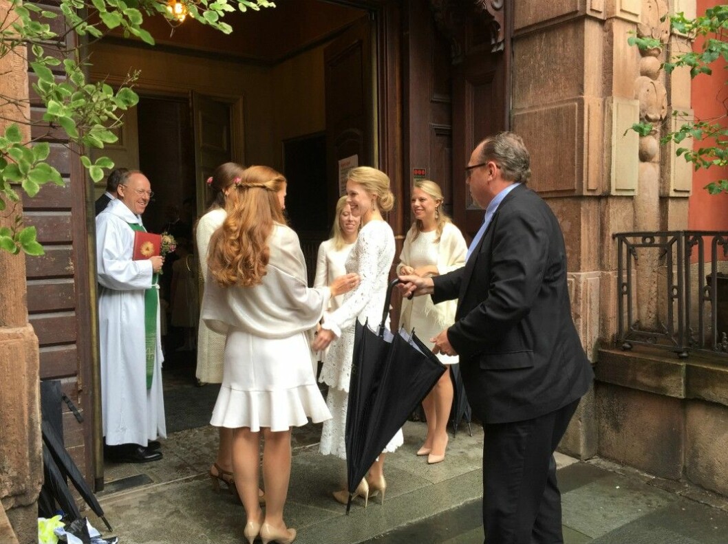 Bruden Erika Widegren anländer till kyrkan. Hon bär en vit spetsklänning med flera volanglager. Istället för slöja har hon dekorerat den blonda uppsättningen med röda blommor.