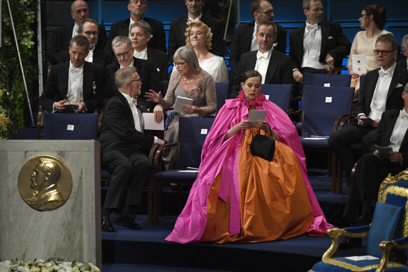 Denna klänning blev Saras allra mest kända. <span class=" italic" data-lab-italic_desktop="italic">”Vi var några som skrek rakt ut när Sara Danius gjorde entré i sin enorma knytbluscape under Nobelprisutdelningen på Konserthusets scen. Drottninglikt skred hon in i sin fantastiska kreation i cerise och brandgult och den bylsigaste taft som gick att tillgå. Och plats för två småväxta Nobelpristagare i litteratur under capen. En påfågel bland pingviner”</span>, skrev Expressen kulturs Gunilla Brodrej.
