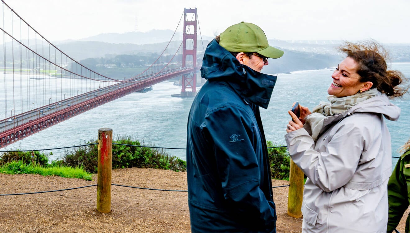 Prins Daniel och kronprinsessan Victoria ler mot varandra vid Golden Gate-bron