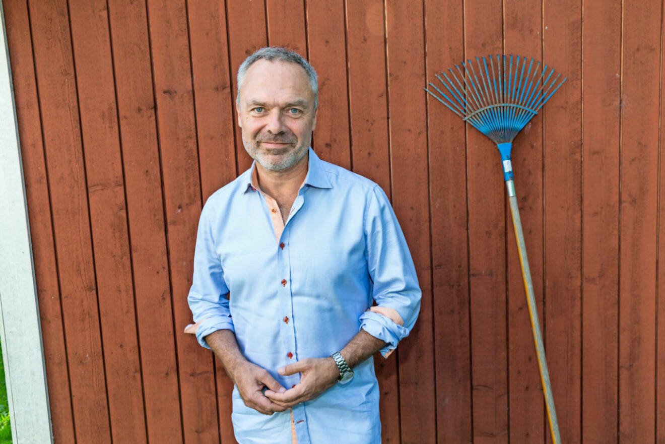 Liberalernas partiledare Jan Björklund poserar i ljusblå skjorta vid rödmålad ytterfasad.