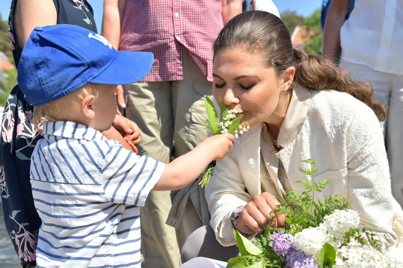 Kronprinsessan Victoria doftar på liljekonvaljer som en liten pojke sträcker fram.