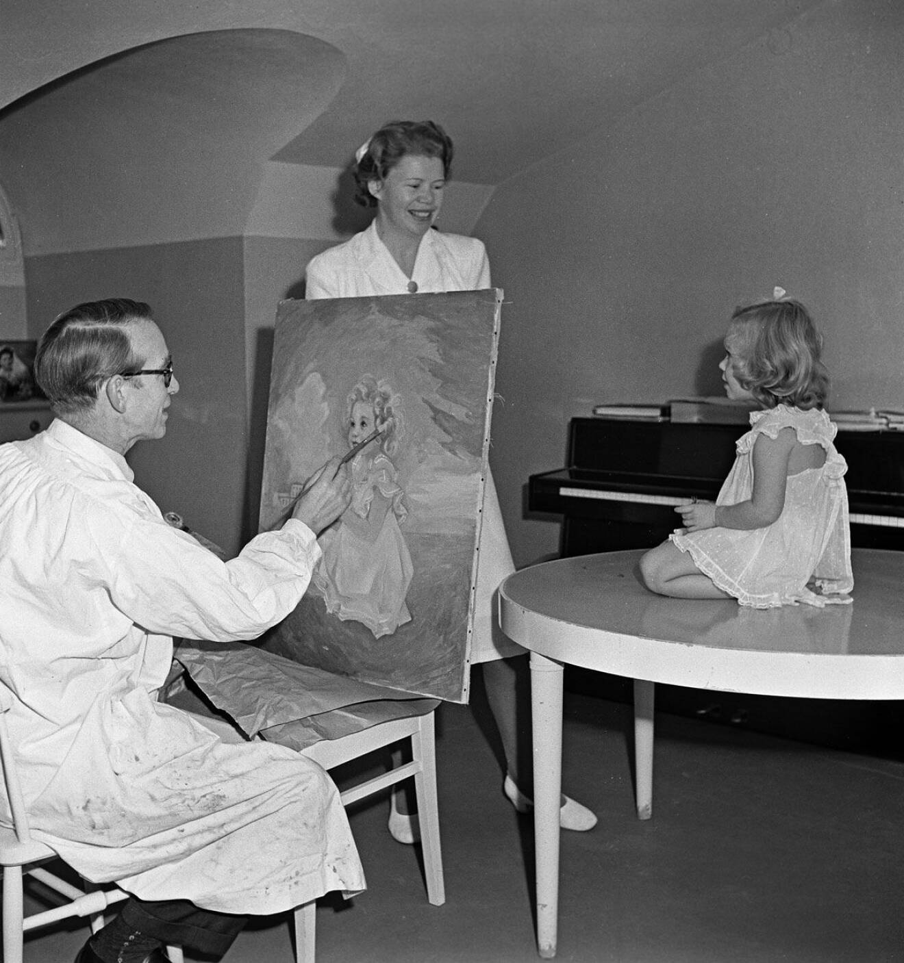 Konstnären Einar Nerman målar av prinsessan Christinas porträtt på Haga slott. Med på bilden är också barnsköterskan Ingrid "Nenne" Björnberg.