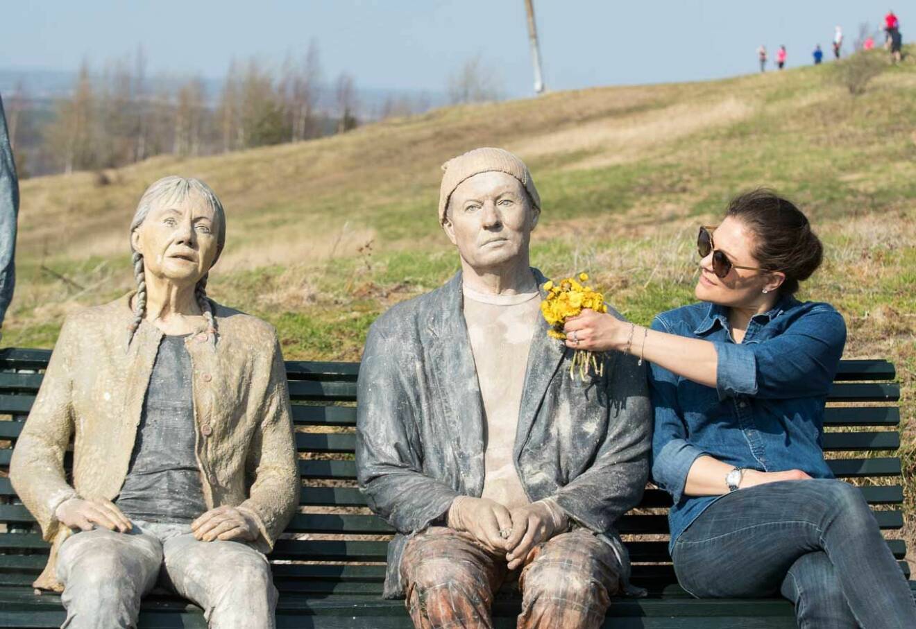 Kronprinsessan Victoria sitter på en parkbänk bredvid en skulptur i form av ett par, under sin landskapsvandring i Närke.