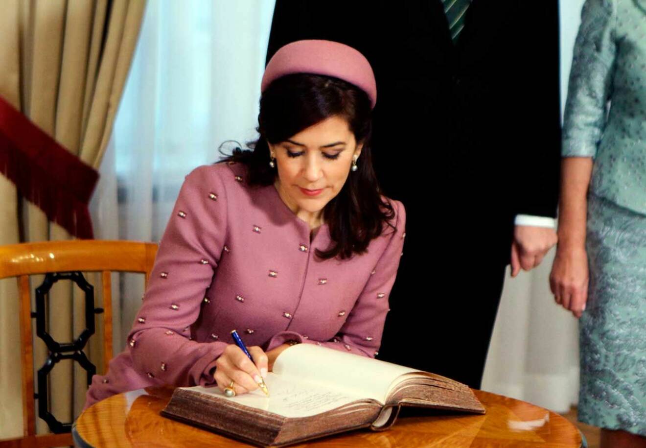 I äkta Jackie Kennedystil bar Mary pillerburkshatt och en fantastisk rosa kappa med små pärlor. Här skriver hon i slottets gästbok.