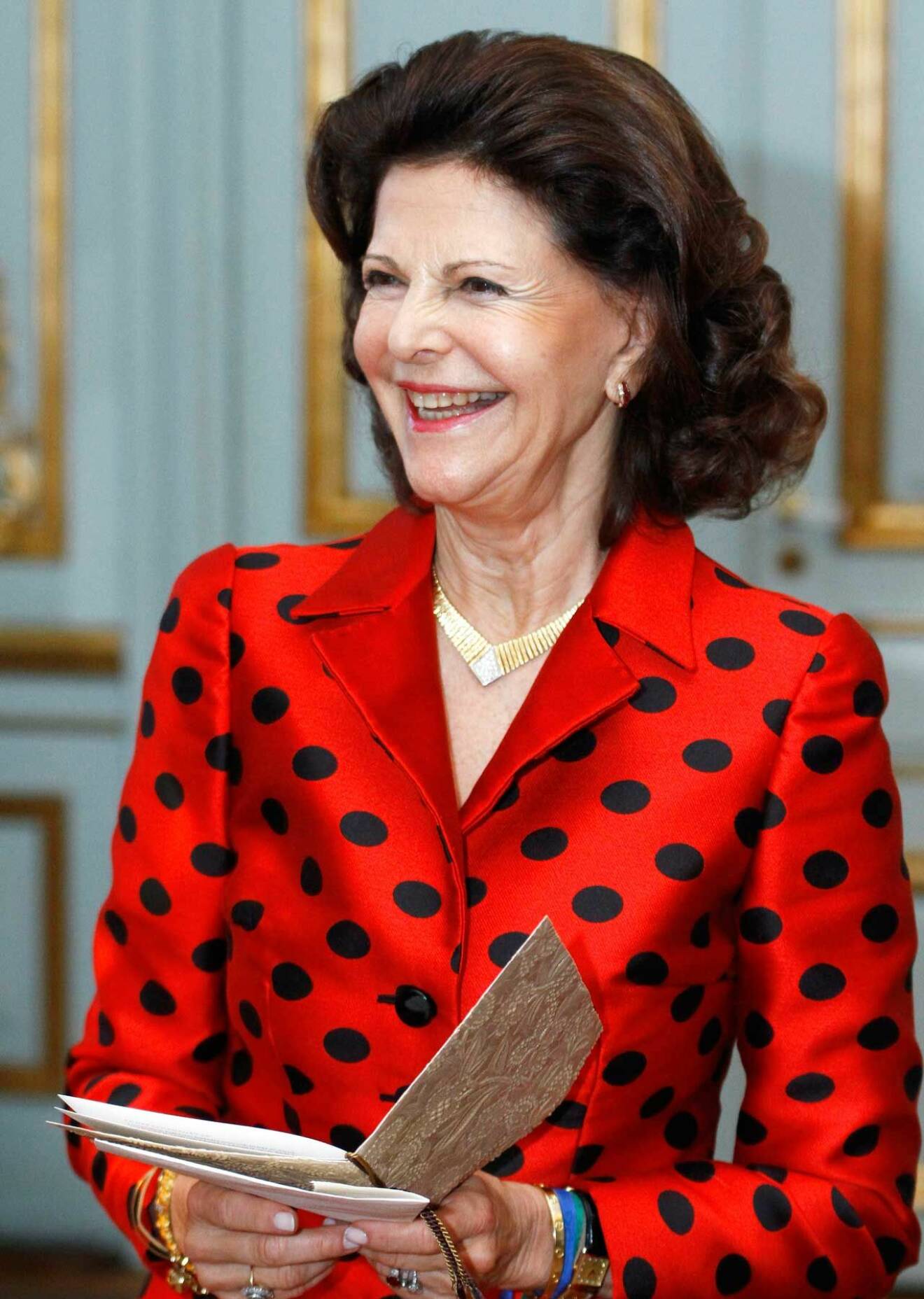 Drottning Silvia på Stockholms slott, klädd i röd prickig sidendräkt.