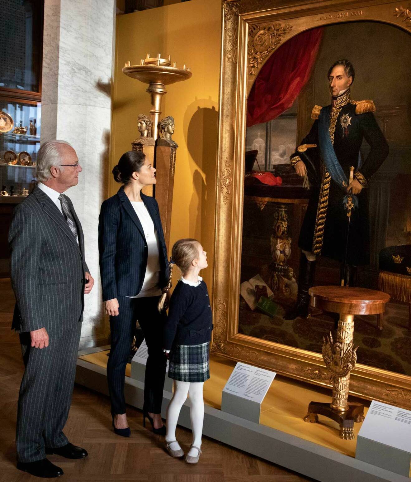Kungen, kronprinsessan Victoria och prinsessan Estelle på Nationalmuseum i Stockholm, framför porträttet av Karl XIV Johan.