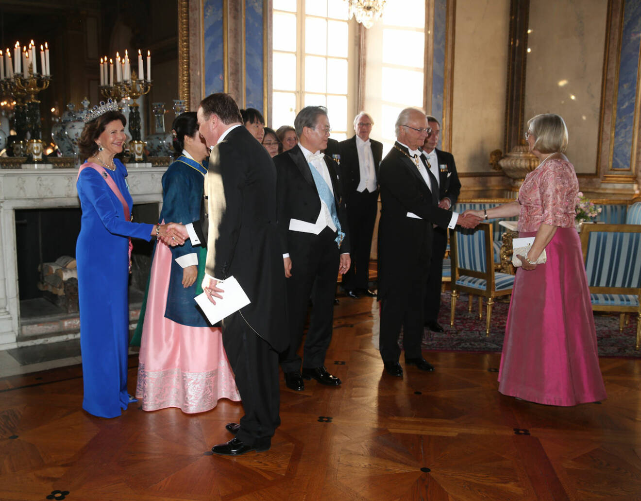 Drottning Silvia i en Korea-blå aftonklänning. Här hälsar hon på statsministern.