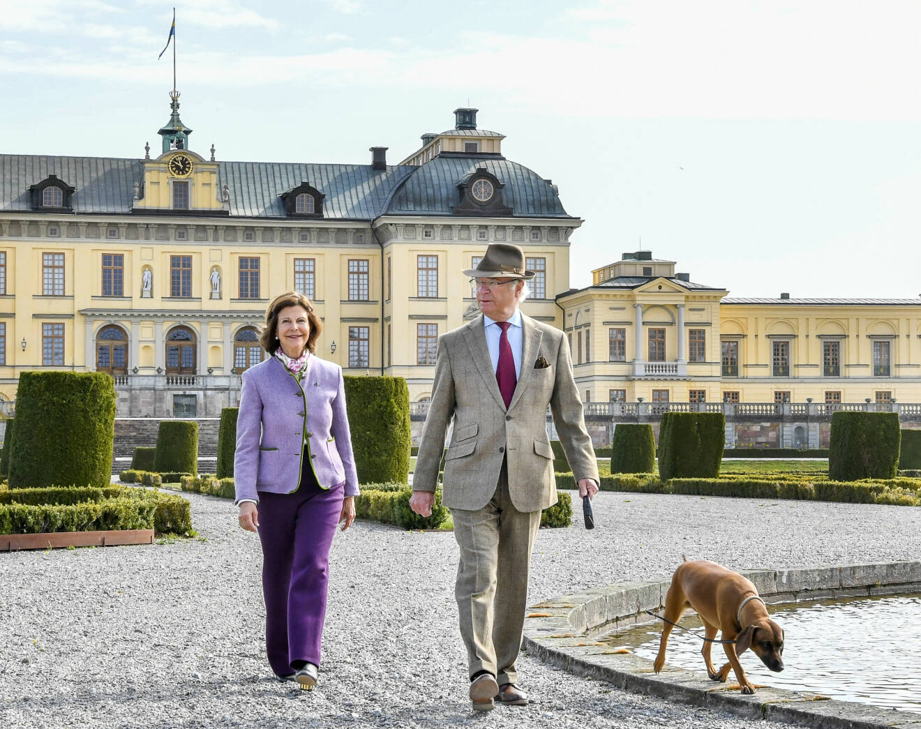 Kungen och drottningen med hunden Brandie framför Drottningholms slott