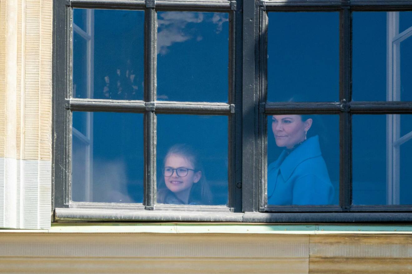 Prinsessan Estelle och kronprinsessan Victoria tittar ut genom ett fönster på Kungliga slottet
