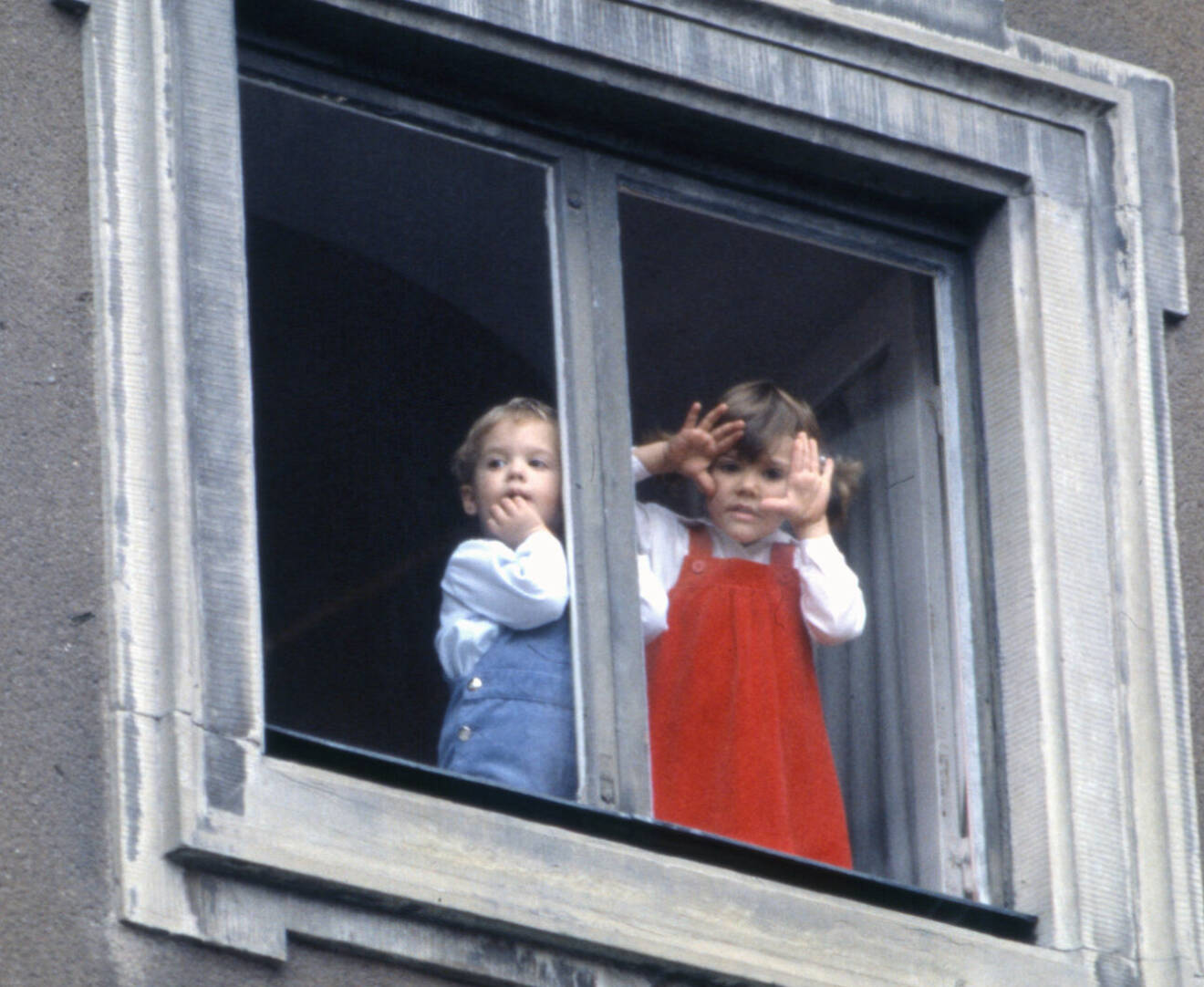 Kronprinsessan Victoria och prins Carl Philip som små, tittar ut genom slottsfönstret