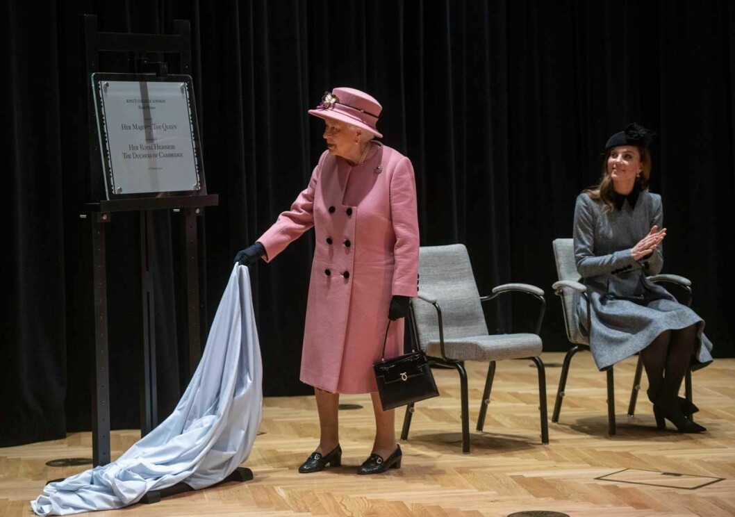 Drottningen invigde, med Kates support. Och spana in deras ”diplomatic dressing”: Kate försvann i stolen, medan drottningen fick stå i fokus i sin rosa kappa. Drottning Elizabeth. Hertiginnan Kate.
