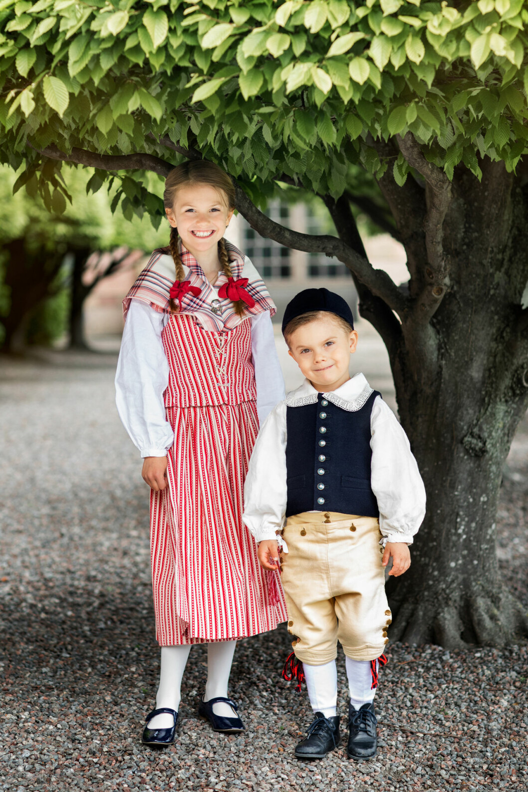 Estelle är polkagrisrandig och fin, och har röda rosetter i flätorna. Och samma röda rosetter går igen i lillebror Oscars knätofsar. Prinsessan Estelle i sin nya folkdräkt från Skedevi. Prins Oscars dräkt är från Ingelstad i Skåne.