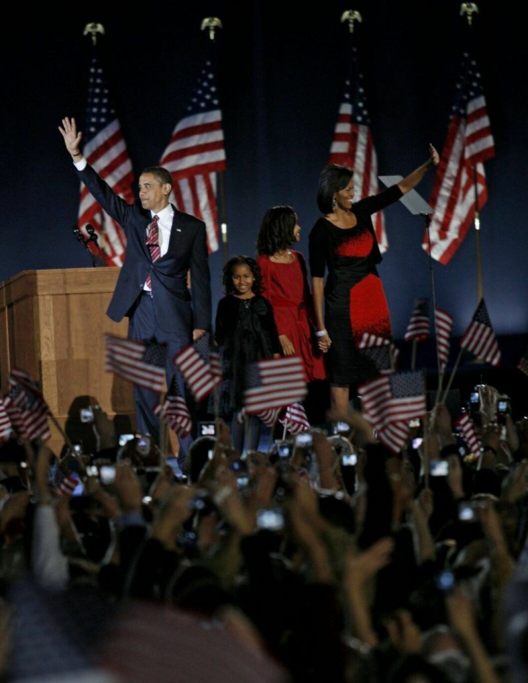 Familjen Obama firar segern i presidentvalet i USA. Familjen Obama står på en scen och vinkar till folkmassorna som viftar med amerikanska flaggor