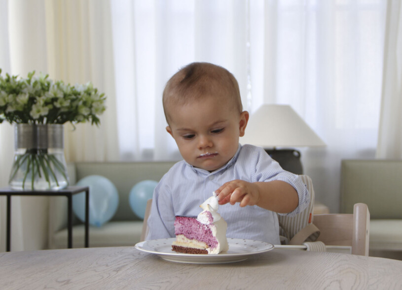 Oscar, 1 år, smaskar tårta i den sociala delen, med soffor, luftiga gardiner och bordlampor. Och så ballonger, dagen till ära! Prins Oscar fyller ett år