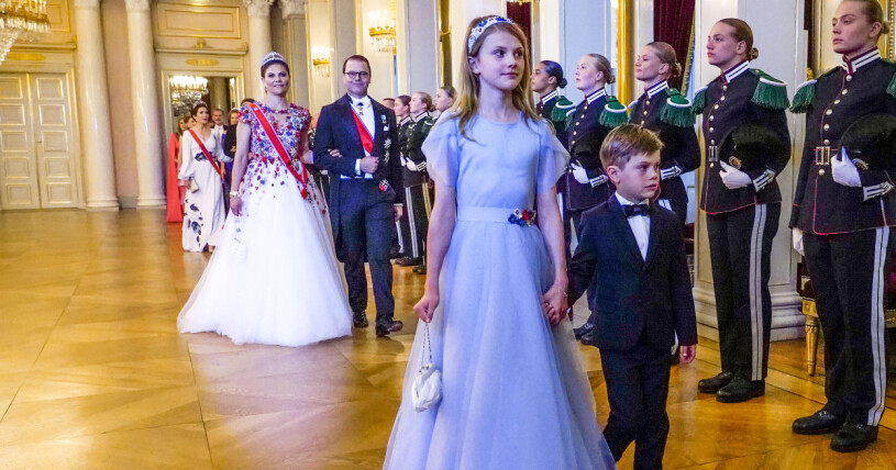 Prinsessan Estelle håller lillebror i handen och leder vägen genom de stora salarna till middagen. Prinsessan Estelle, prins Oscar, kronprinsessan Victoria och prins Daniel