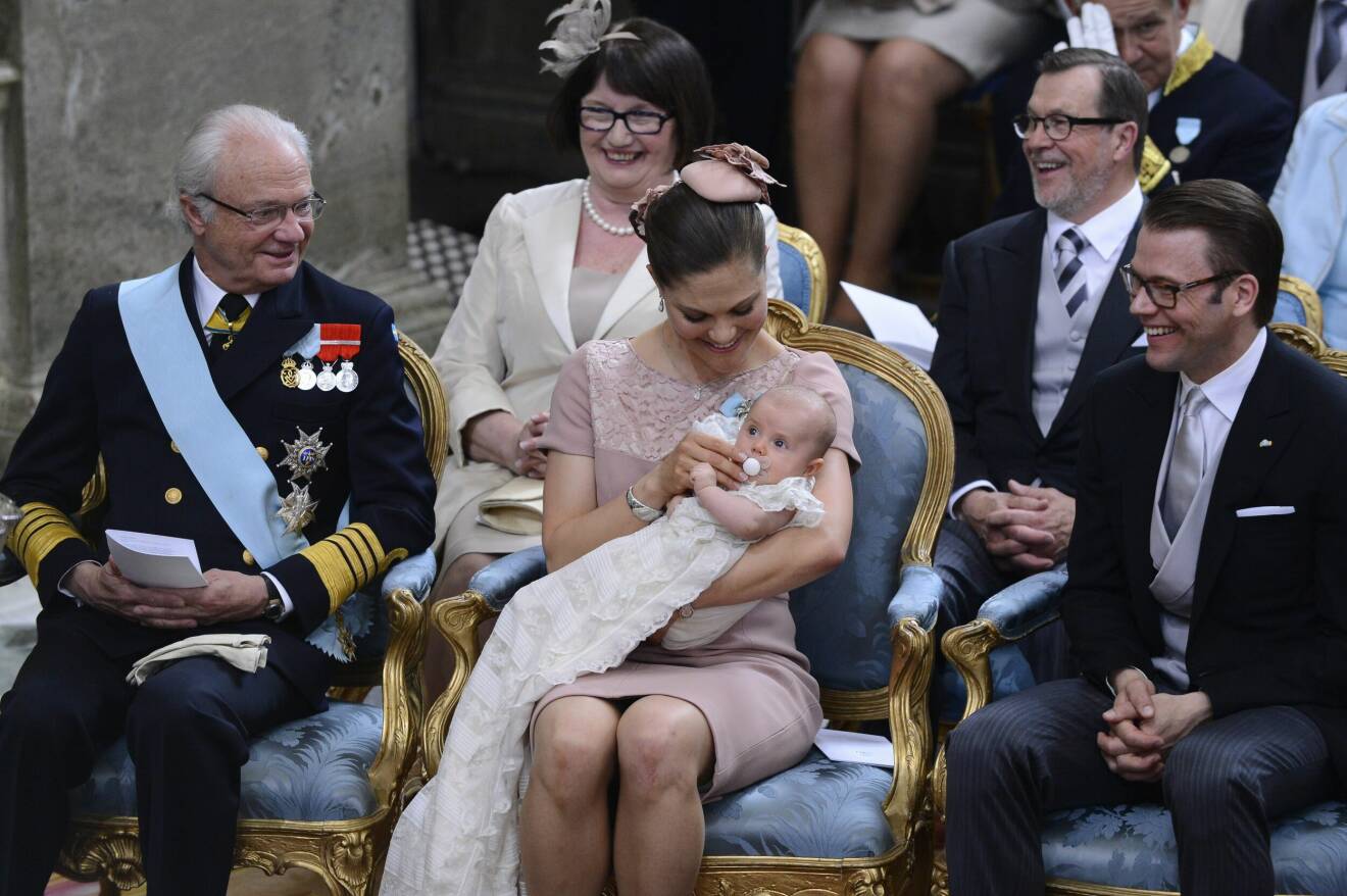 kung Carl XVI Gustaf, kronprinsessan Victoria och prins Daniel ler när prinsessan Estelle får sin napp under dopceremonin i Slottskyrkan på tisdagen (Ewa Westling och Olle Westling i bakgrunden).