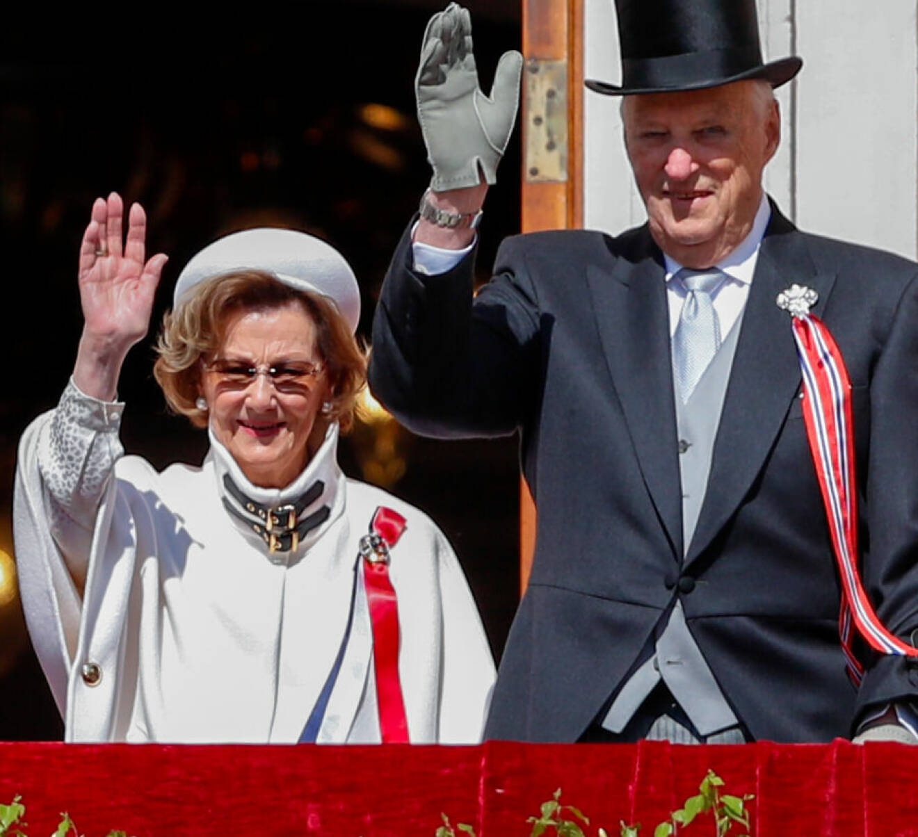 Kung Harald och drottning Sonja vinkar från slottsbalkongen under nationaldagsfirandet 2023