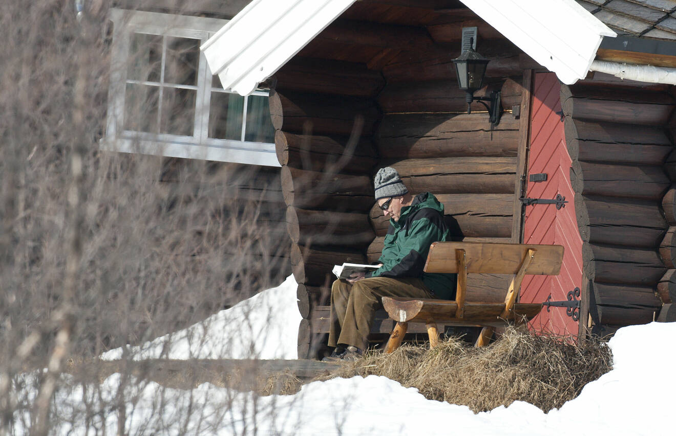 Kung Harald läser en bok i solen framför Prinsehytta i Sikkilsdalen