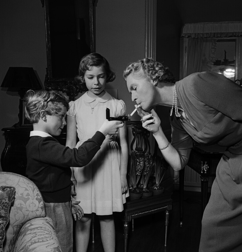 1953. Kungen var sju år och prinsessan Christina var tio. Kungen, då kronprins, tänder mamma prinsessan Sibyllas cigarett medan prinsessan Christina ser på