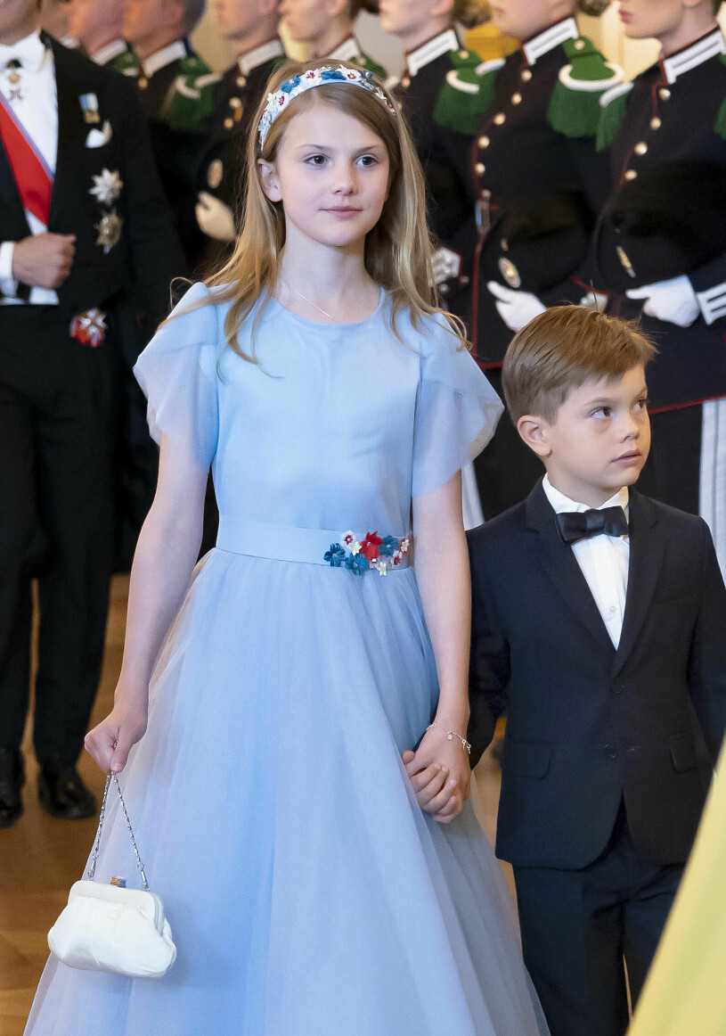 Prinsessan Estelle med en av alla sina handväskor – och med lillebror förstås. Prinsessan Estelle i ljusblå aftonklänning och med vit aftonväska handväska