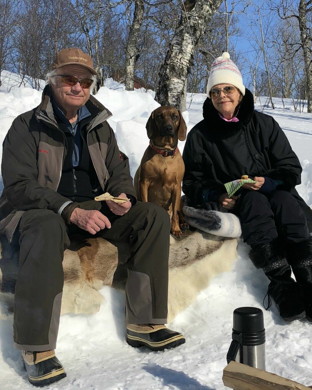 Termoskaffe och kaka i vårsolen! Kung Carl Gustaf och drottning Silvia och hunden Brandie firar påsk i Storlien våren 2018. På utflykt, de sitter på ett renskinn och har med sig termos.