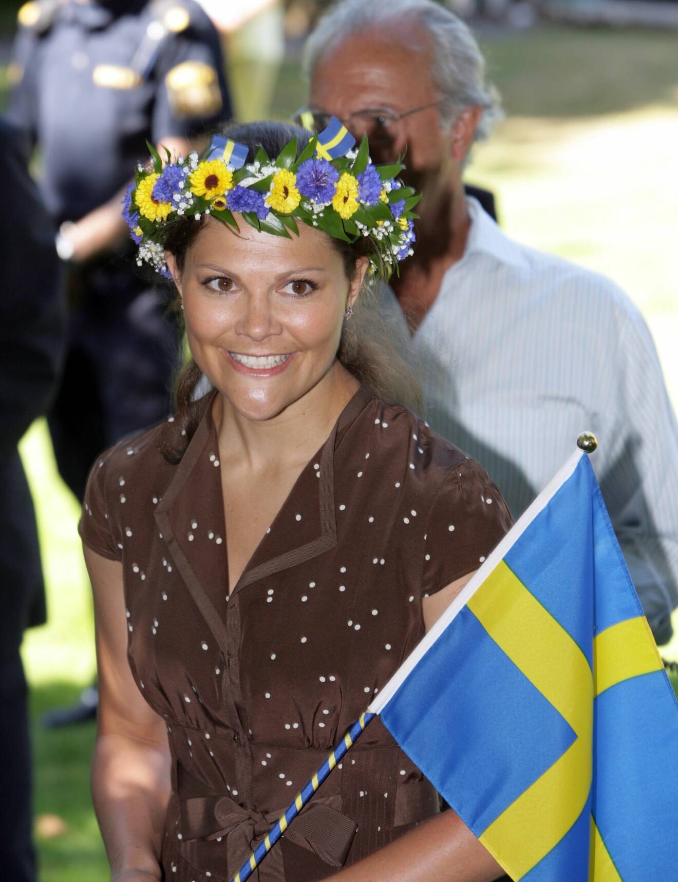 Kronprinsessan Victoria i blomsterkans och med en Sverige-flagga i handen