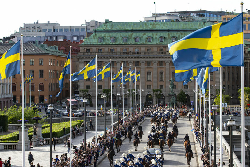 Nationaldagskortegen på väg över Norrbro, med de svenska flaggorna vajande i vinden. Den kungliga kortegen under nationaldagen 2022
